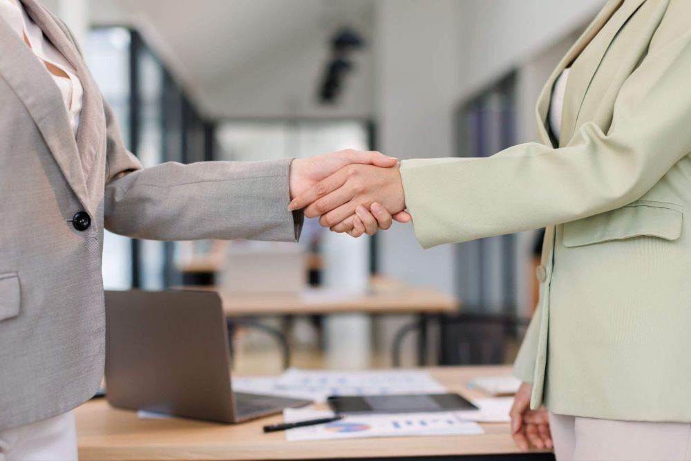 two people shaking hands in front of a laptop