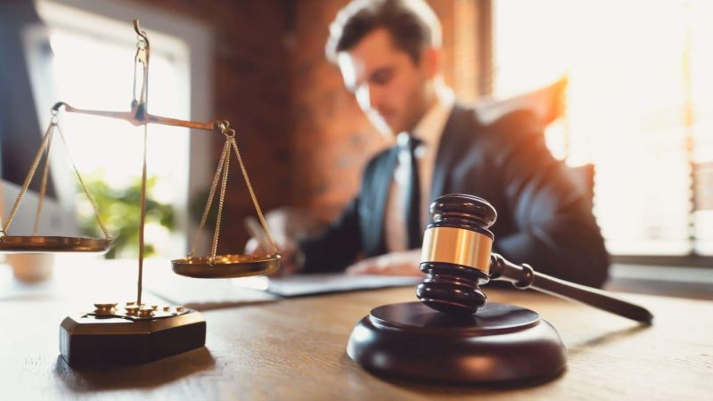 a man in a suit and tie sitting at a desk with a scale of justice