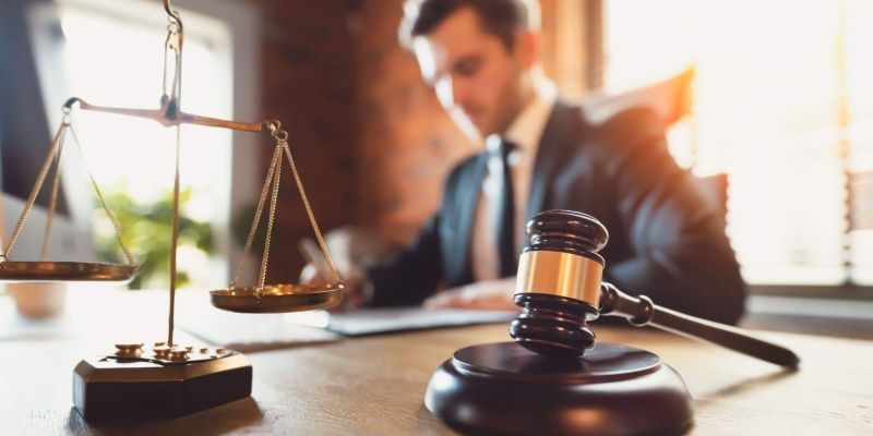 a man in a suit and tie sitting at a desk with a scale of justice