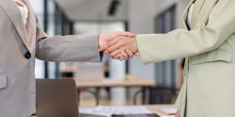 two people shaking hands in front of a laptop