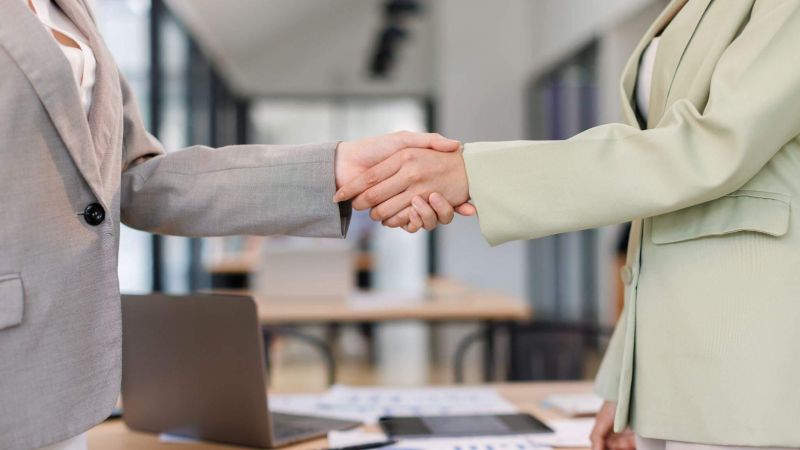 two people shaking hands in front of a laptop